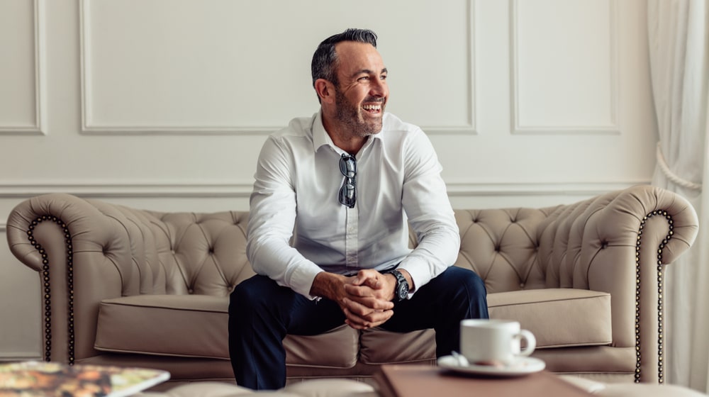 The gentleman in the white shirt is sitting on a two-seater and smiling