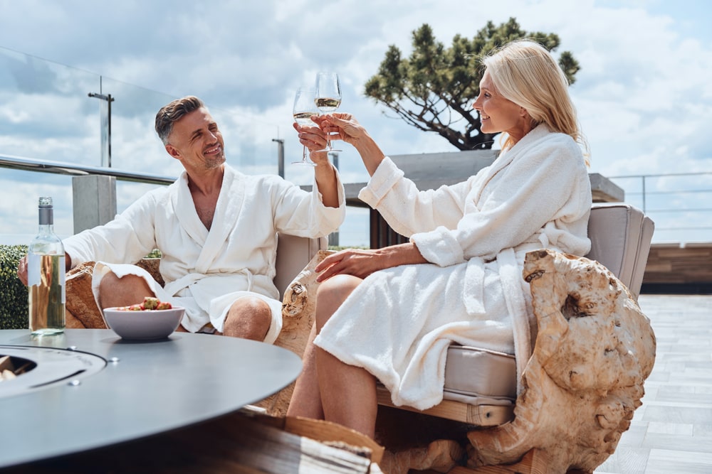 Beautiful luxury couple in bathrobes enjoys fruits and wine while relaxing in luxury hotel outdoors