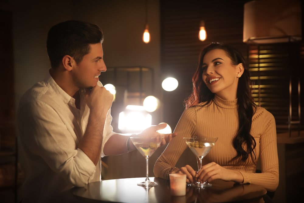 Ein Mann und eine Frau sitzen an einem Tisch mit Martini-Gläsern, lächeln und genießen ihr Getränk auf Zuckerguss