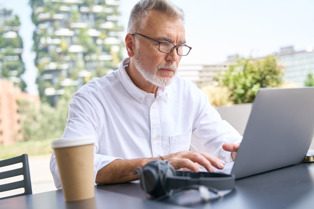 Older senior business man using laptop elearning sitting outside. 60 years old adult professional businessman working online on computer,