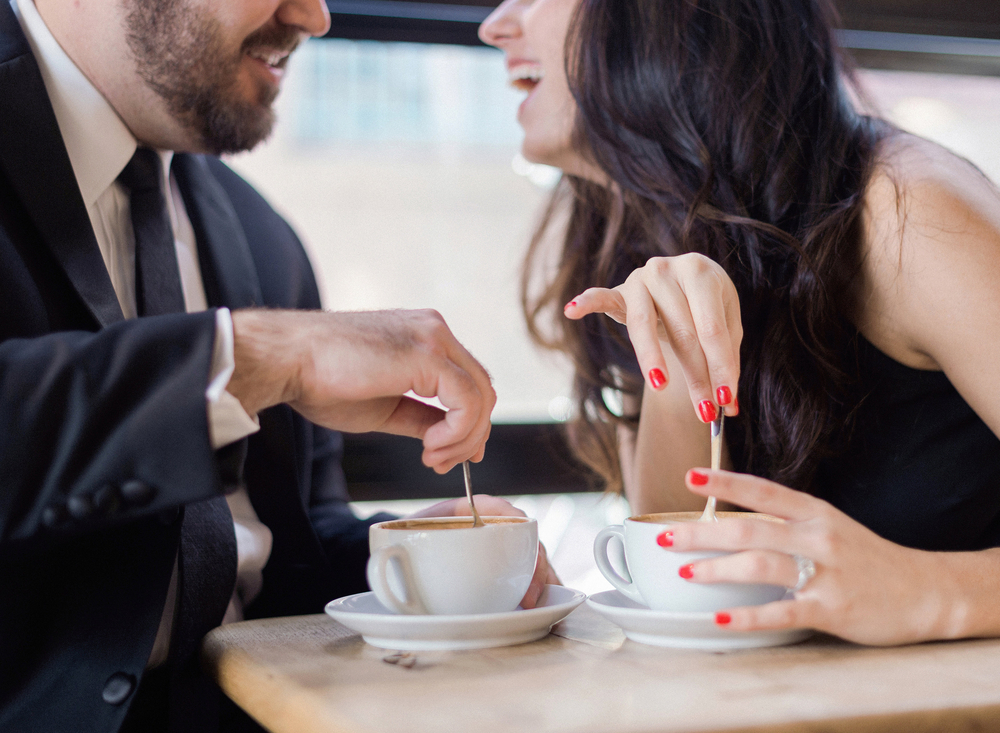 Lächelndes Paar bei einem Date im Café, rührt Kaffee um und unterhält sich entspannt.