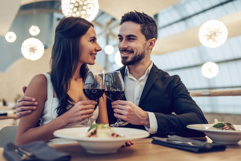 Elegantes Paar genießt ein romantisches Abendessen im Luxusrestaurant, lächelt und stößt mit Rotwein an.