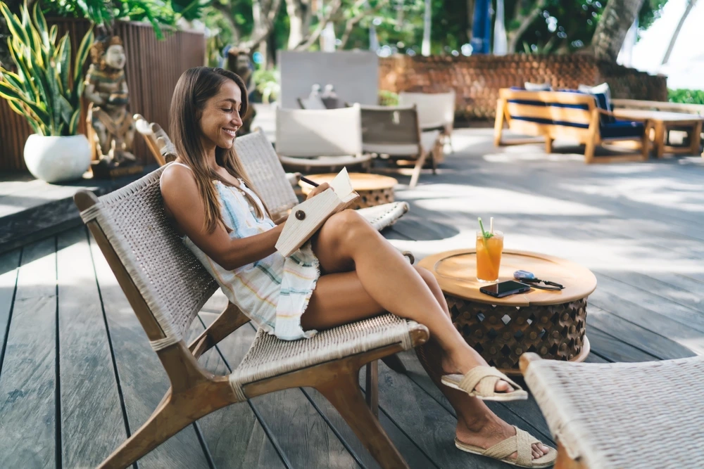Woman relaxing outdoors reading a book with a cocktail beside her