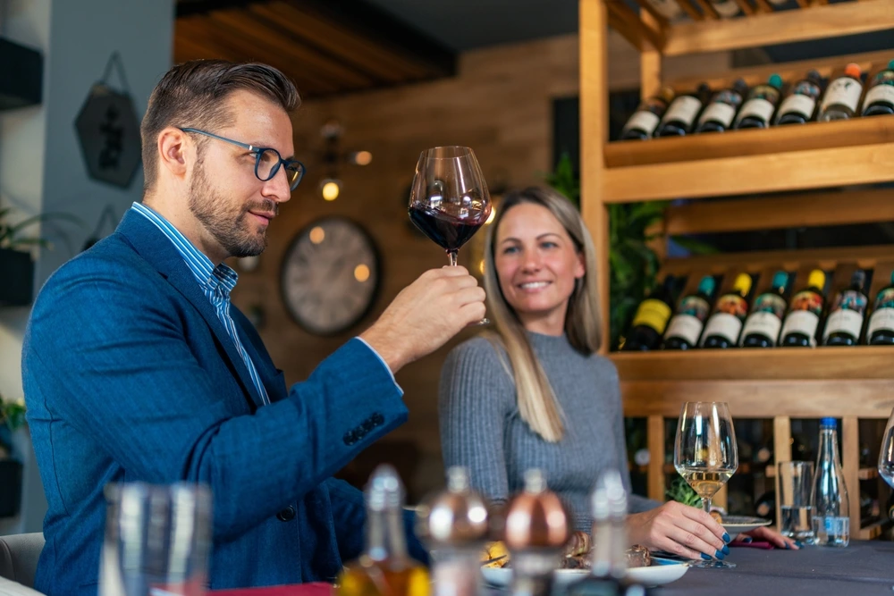 Paar beim ersten Date im Restaurant, er hebt ein Glas Rotwein, sie lächelt – romantische Atmosphäre