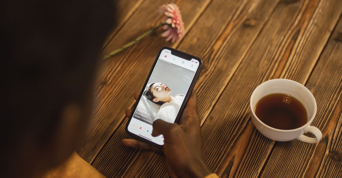 Eine Person nutzt eine Dating-App auf dem Smartphone, daneben steht eine Tasse Tee auf einem Holztisch.